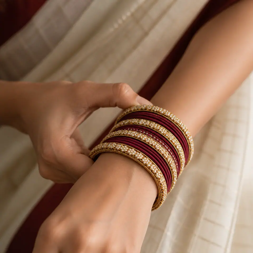 Wrist stacking a maroon silk thread and kundan bangle set above a cotton saree